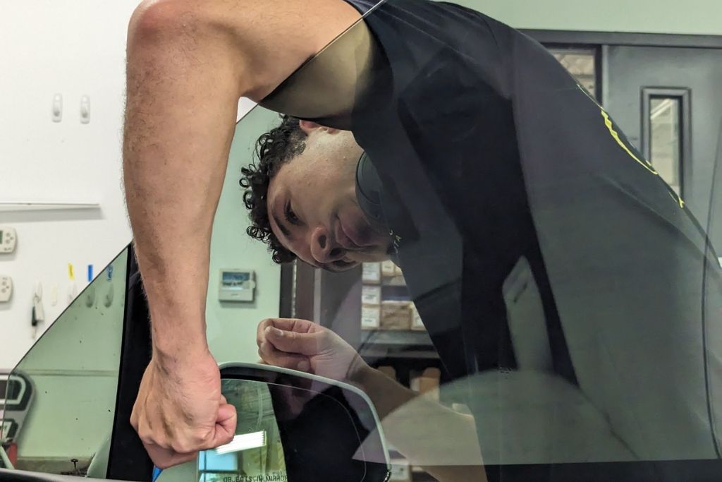 A technician carefully applies window tint film to a car window using a squeegee, ensuring a smooth, bubble-free finish. The image captures the precision and attention to detail involved in professional tint installation.
