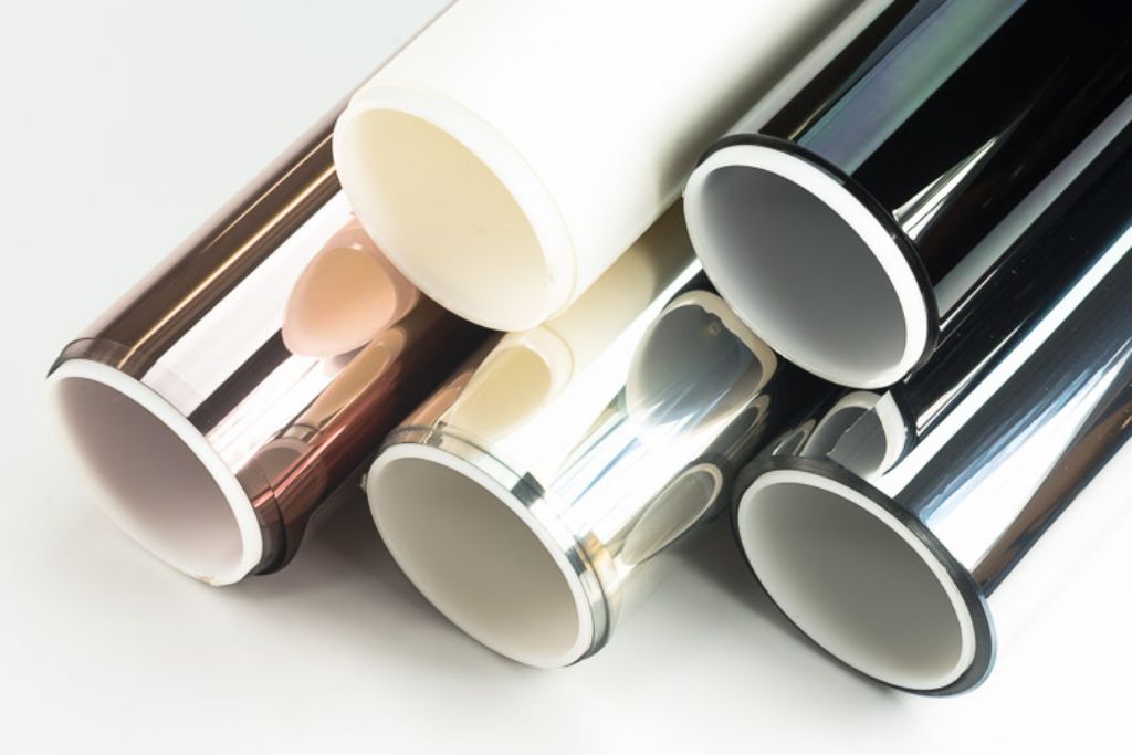 Close-up view of five rolled window tint films in various shades, including bronze, silver, and black, showcasing different tint materials and finishes. The reflective surfaces highlight the variety of options available for car window tinting.