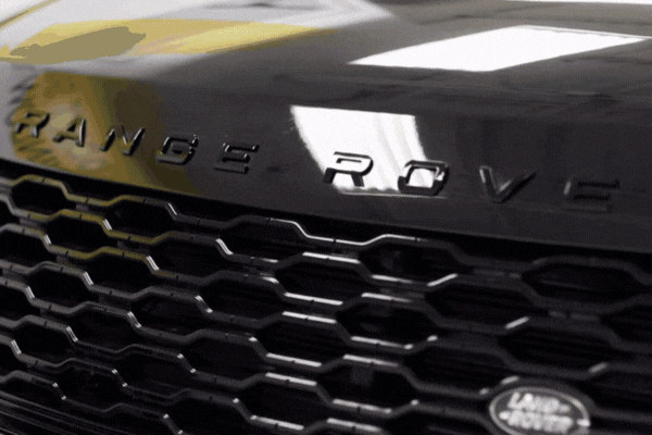Close-up animation of a black Range Rover grille with shiny honeycomb pattern and reflective hood surface, showing the vehicle’s logo in motion as light shifts across it.